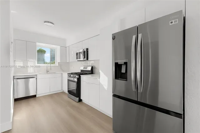 a kitchen with stainless steel appliances a refrigerator a sink a stove and white cabinets