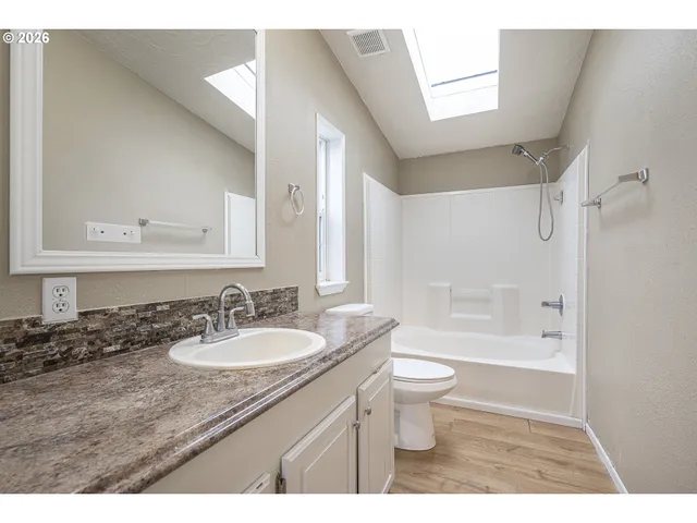 a bathroom with a granite countertop sink a toilet a mirror a bathtub and shower