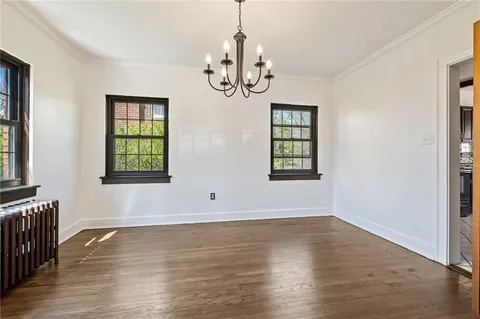 an empty room with wooden floor chandelier and windows