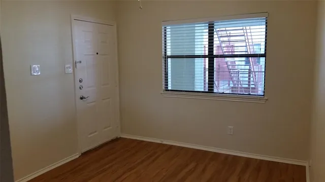 a view of an empty room with wooden floor and a window