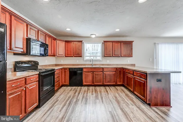 a kitchen with stainless steel appliances granite countertop wooden cabinets a stove top oven a sink and dishwasher a oven with wooden floor