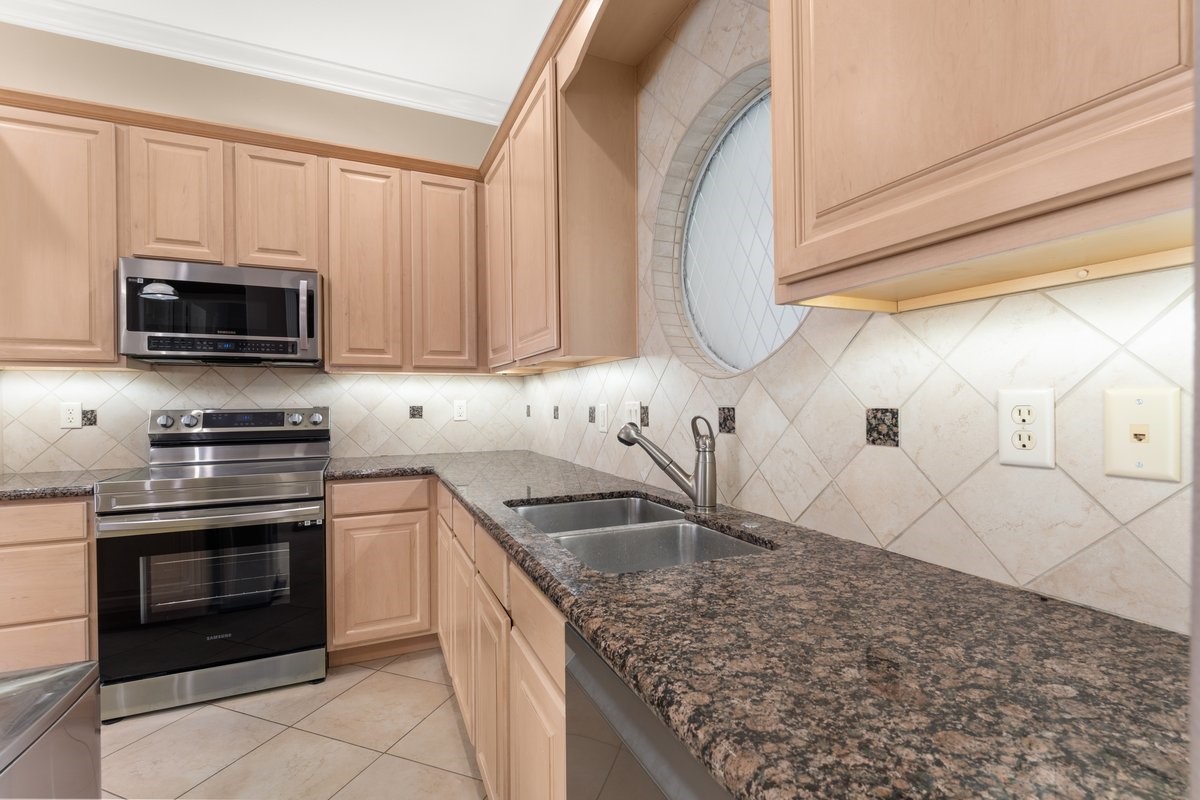 168 Lake Point Boulevard, Unit C102 Conroe, TX 77356 - Photo 5 of 35 This kitchen features modern stainless steel appliances, granite countertops, light wood cabinets, and a unique circular window, offering a blend of style and functionality.