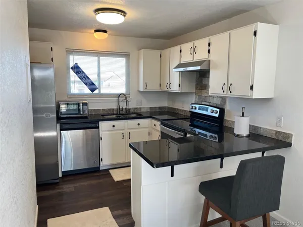 a kitchen with stainless steel appliances granite countertop a stove a sink dishwasher a refrigerator a microwave oven with white cabinets and wooden floor