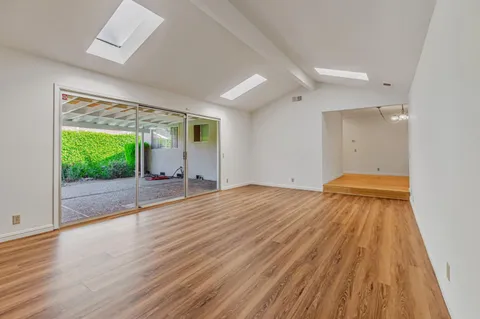 an empty room with wooden floor chandelier fan and windows