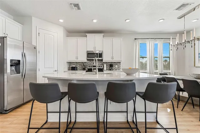 a kitchen with stainless steel appliances granite countertop a stove top oven a sink a dining table and chairs with wooden floor