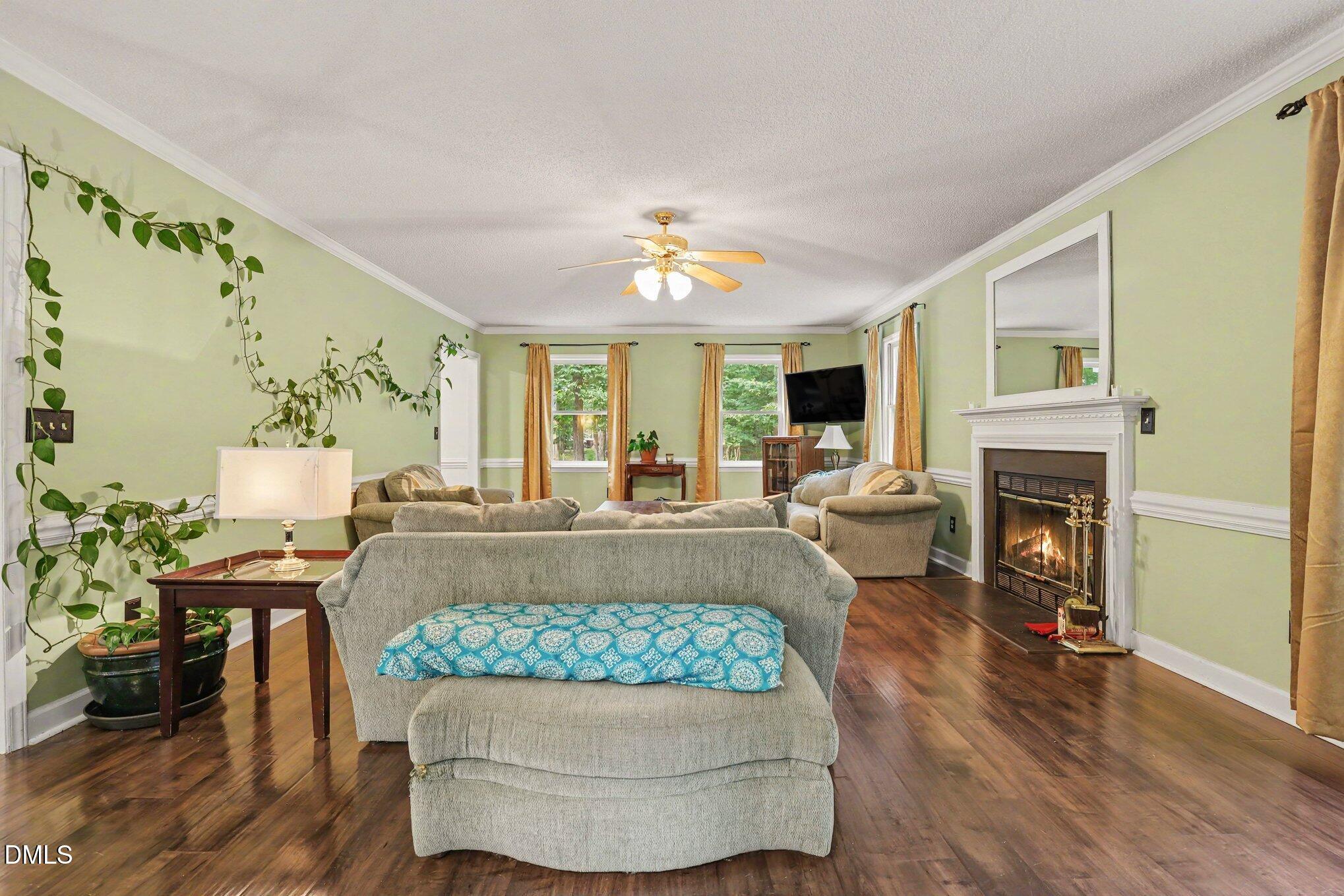 114 Oak Hollow Road Timberlake, NC 27583 - Photo 8 of 31 Spacious living area featuring wood-finish flooring, a traditional fireplace with white mantel, crown molding, and a ceiling fan