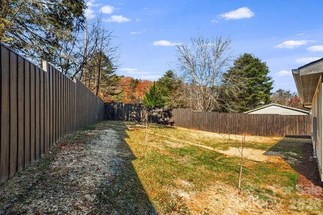 a view of backyard with large trees and wooden fence