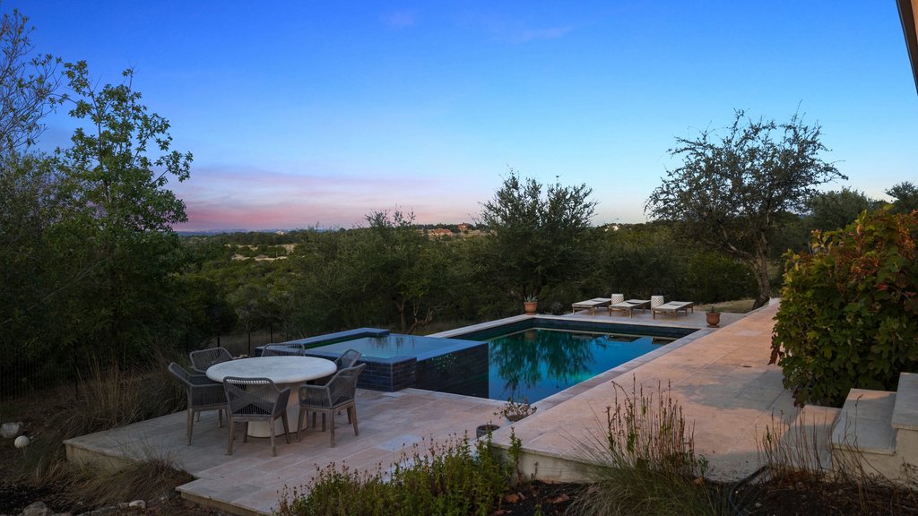 32045 Mirela Ann Road Dripping Springs, TX 78620 - Photo 1 of 30 An inviting swimming pool and integrated spa sit surrounded by stone decking overlooking lush green hills.