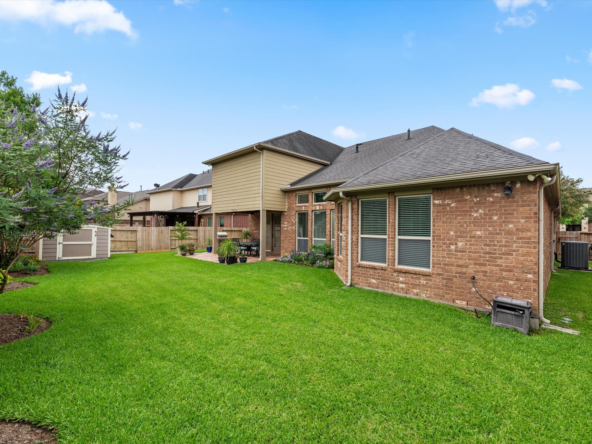 3907 Randle Ridge Court Fulshear, TX 77441 - Photo 36 of 46 Spacious backyard with lush green lawn, a brick exterior, large windows, and a patio area, ideal for outdoor relaxation and gatherings.