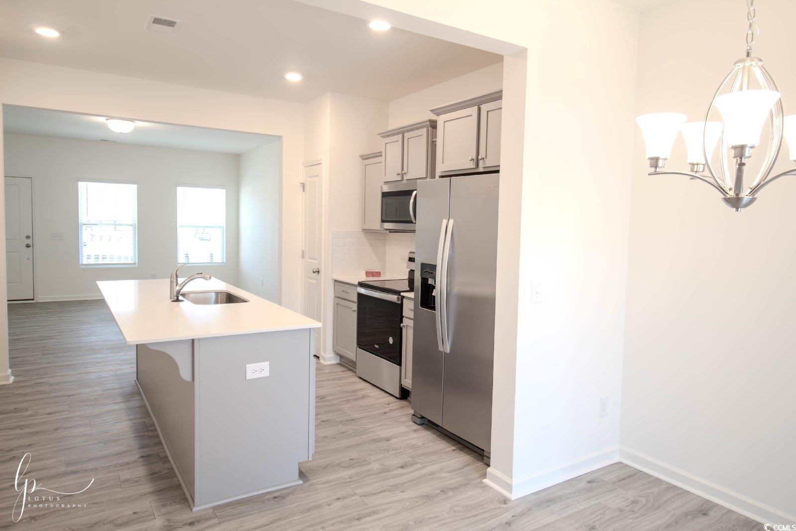 172 Crescent Way Little River, SC 29566 - Photo 6 of 18 Kitchen with stainless steel appliances, a sink, light countertops, light wood-style flooring, and a kitchen island with sink