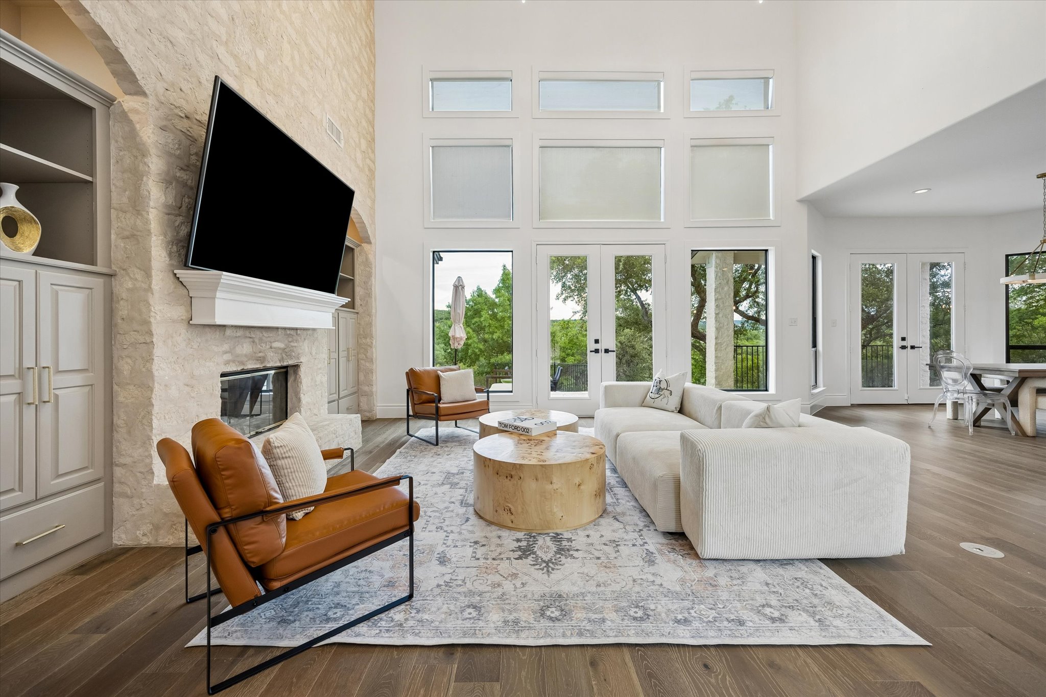 3719 Bee Creek Road Spicewood, TX 78669 - Photo 8 of 40 A spacious living area features lofty ceilings, a stone fireplace, and abundant natural light from numerous windows and French doors.