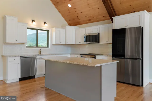 a kitchen with stainless steel appliances granite countertop a refrigerator a sink a stove a microwave and island with wooden floor