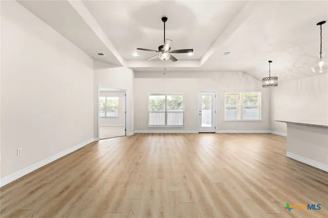 an empty room with wooden floor chandelier and windows
