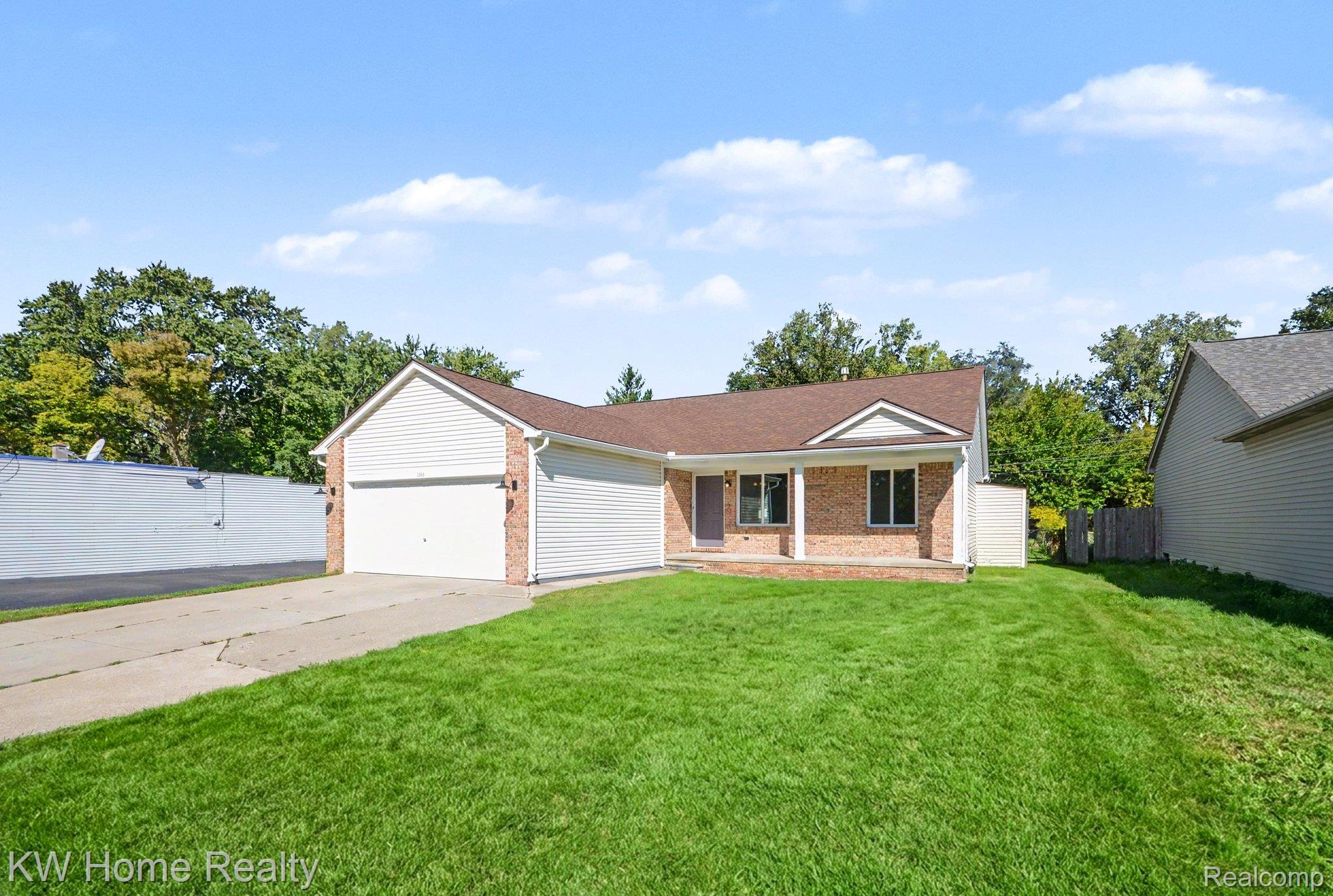 2383 East Maple Road Troy, MI 48083 - Photo 2 of 25 Exterior featuring brick accents, white siding, an attached garage, a covered front entry, and a paved driveway