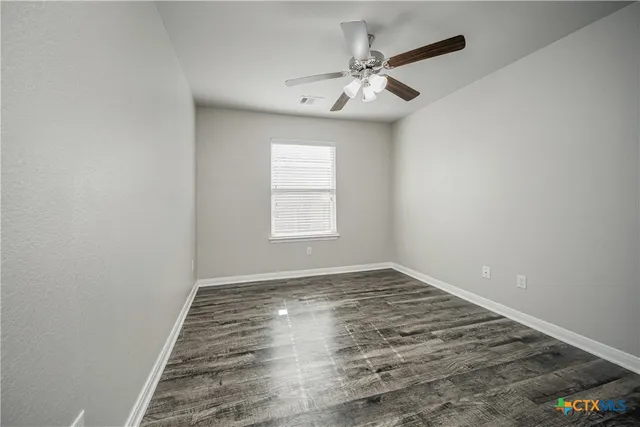 an empty room with wooden floor fan and windows