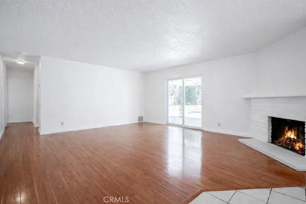 a view of an empty room with wooden floor fireplace and a window