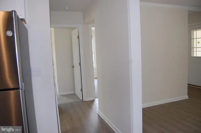 a view of hallway with a refrigerator and wooden floor