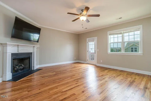 a view of an empty room with wooden floor fireplace and a window
