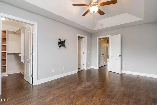 a view of an empty room with wooden floor and a ceiling fan