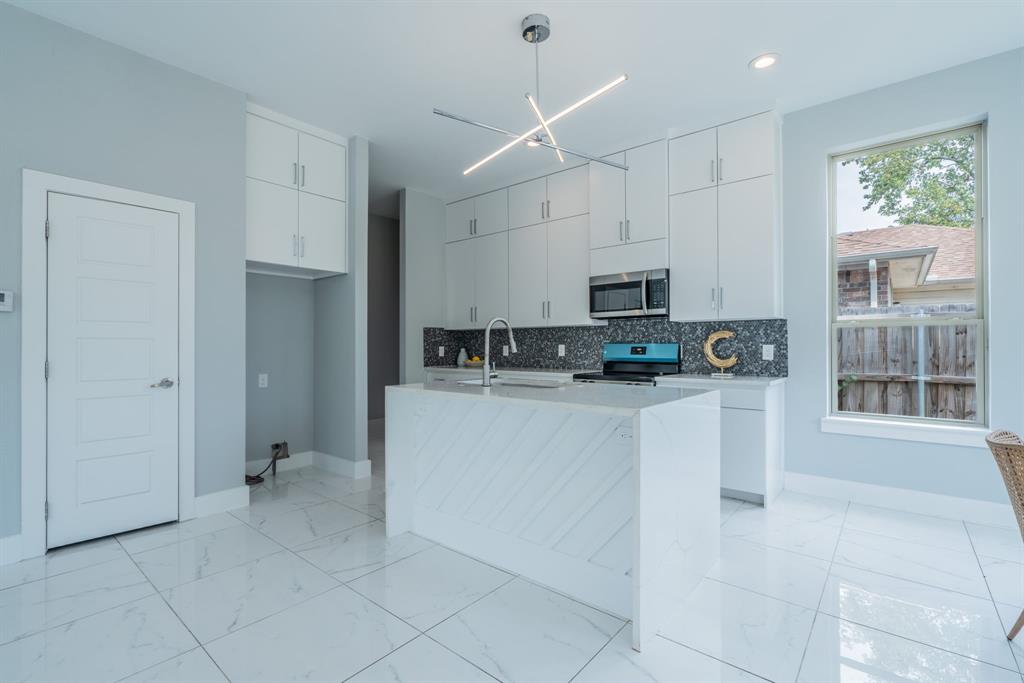 3610 Vilbig Road Dallas, TX 75212 - Photo 6 of 29 Kitchen featuring white cabinetry, a central island with a waterfall edge, stainless steel appliances, and large format floor tiling