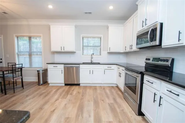 a kitchen with stainless steel appliances granite countertop a sink dishwasher a stove top oven a refrigerator with white cabinets and wooden floor