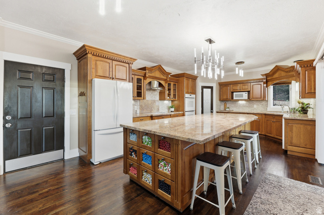 2342 Charros Road Sandy, UT 84092 - Photo 20 of 94 Spacious kitchen featuring rich wood cabinetry, stone countertops, a large center island with seating, dark wood-finish flooring, and a decorative chandelier