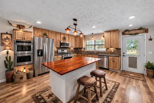 a kitchen with stainless steel appliances granite countertop a refrigerator a sink dishwasher a stove and a dining table with wooden floor