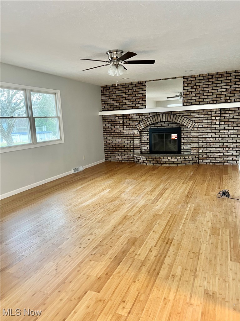 15317 Strader Road East Liverpool, OH 43920 - Photo 10 of 23 Unfurnished living room featuring ceiling fan, light hardwood / wood-style floors, brick wall, and a brick fireplace