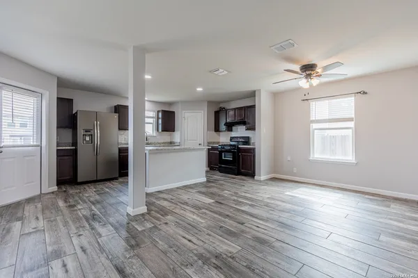 an empty room with wooden floor kitchen view and a window