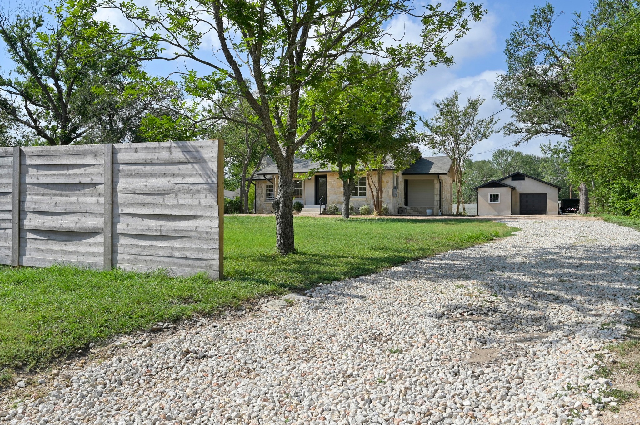 3501 Pecan Springs Road Austin, TX 78723 - Photo 2 of 40 View of front of house featuring an outbuilding, a front yard, gravel driveway, a detached garage, and stone siding