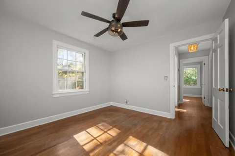 an empty room with wooden floor fan and windows