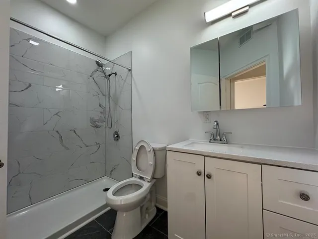 a bathroom with a granite countertop toilet sink shower and mirror