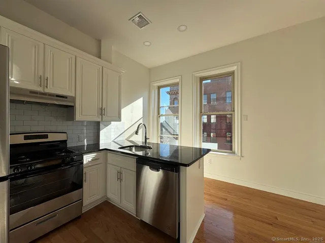 a kitchen with stainless steel appliances granite countertop a sink a stove and a wooden floors
