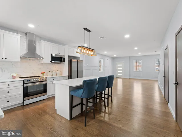 a kitchen with stainless steel appliances kitchen island granite countertop a stove a sink a refrigerator and a dining table with wooden floor