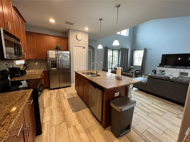 a kitchen with stainless steel appliances kitchen island granite countertop a refrigerator a stove top oven a sink dishwasher and wooden cabinets