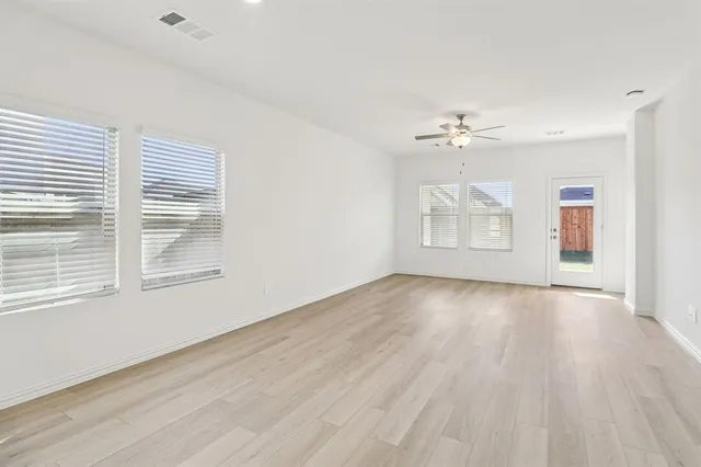 an empty room with wooden floor chandelier fan and windows