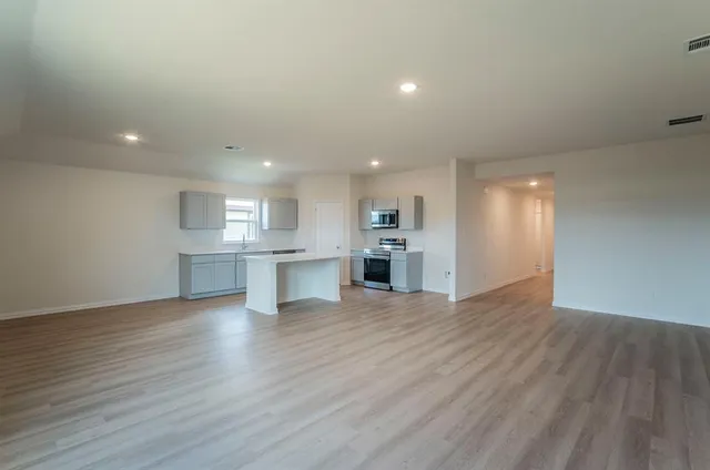 an empty room with wooden floor kitchen view and windows