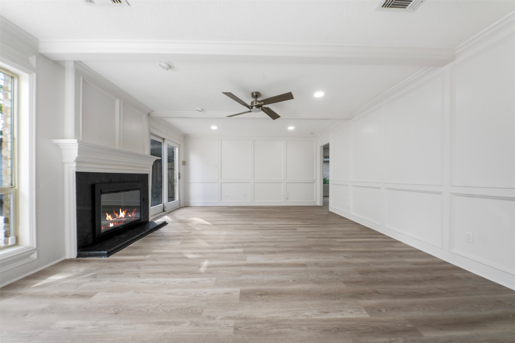 9543 Enstone Circle Spring, TX 77379 - Photo 6 of 50 Spacious living room with elegant white walls and wood-like flooring. Features a cozy fireplace, large windows for natural light, a ceiling fan, and recessed lighting, creating a warm and inviting atmosphere.