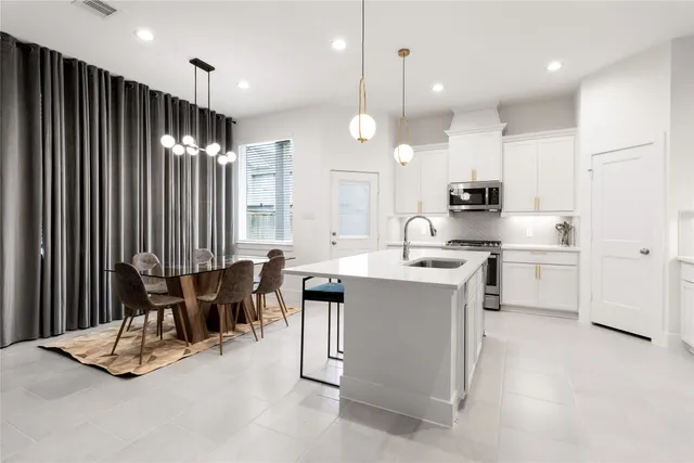 a kitchen with kitchen island stainless steel appliances a table chairs sink and stove top oven