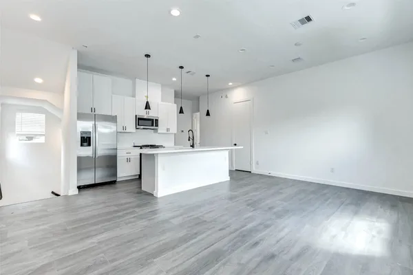 a large white kitchen with kitchen island a sink dishwasher a stove and white cabinets with wooden floor