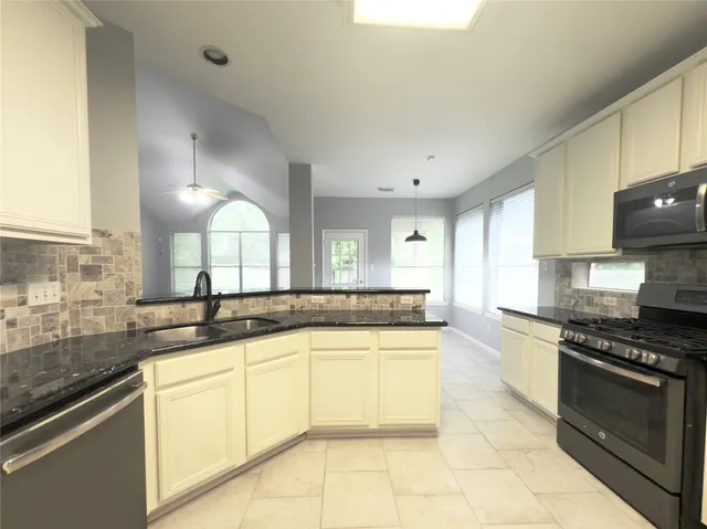 a kitchen with granite countertop a sink stainless steel appliances and white cabinets
