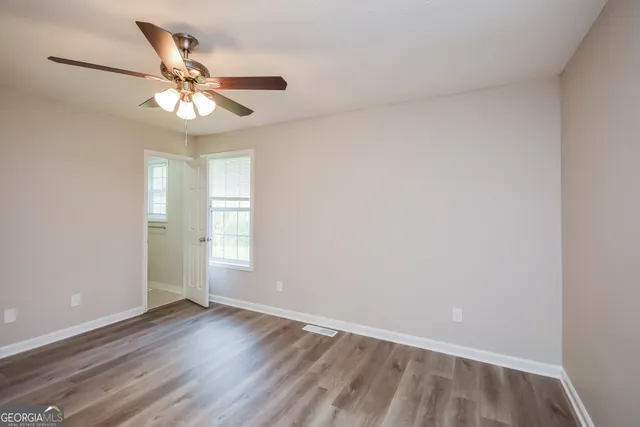 an empty room with wooden floor fan and windows