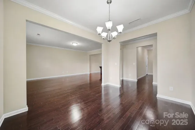 a view of an empty room with wooden floor and chandelier