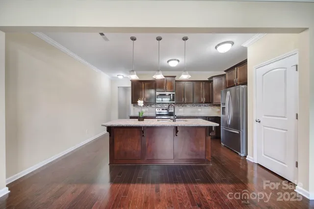 a kitchen with stainless steel appliances granite countertop a refrigerator a sink dishwasher a stove and white countertops with wooden floor