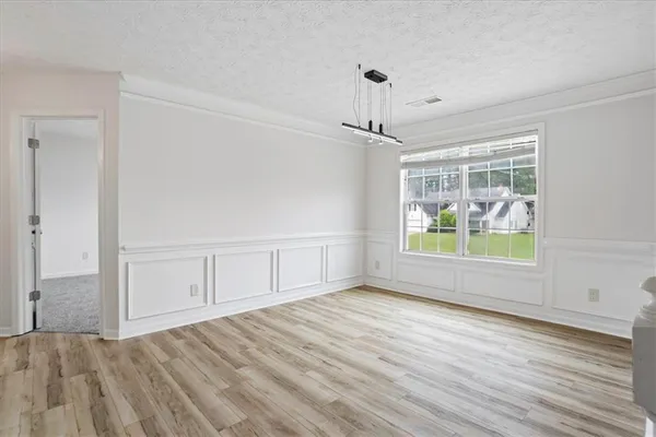 a view of an empty room with window and hardwood floor