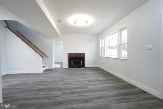 a view of an empty room with wooden floor fireplace and a window