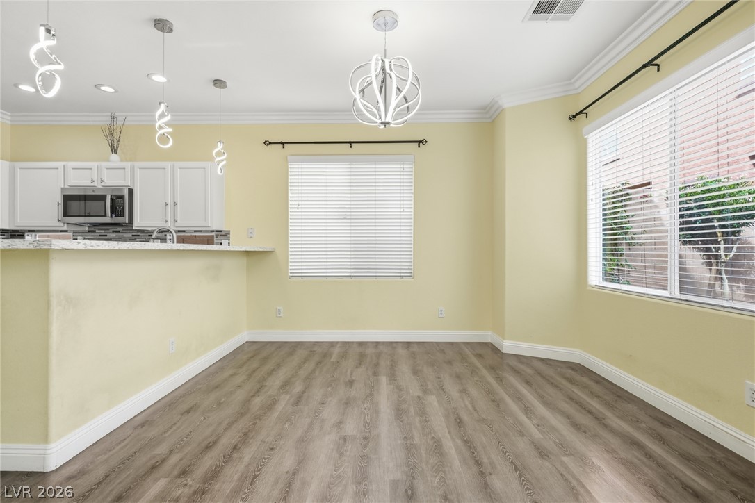 8932 Caledon Ridge Court Las Vegas, NV 89149 - Photo 20 of 39 Plank flooring and crown molding frame a sunlit dining area beside the open kitchen.