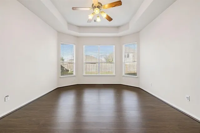 an empty room with wooden floor chandelier fan and windows