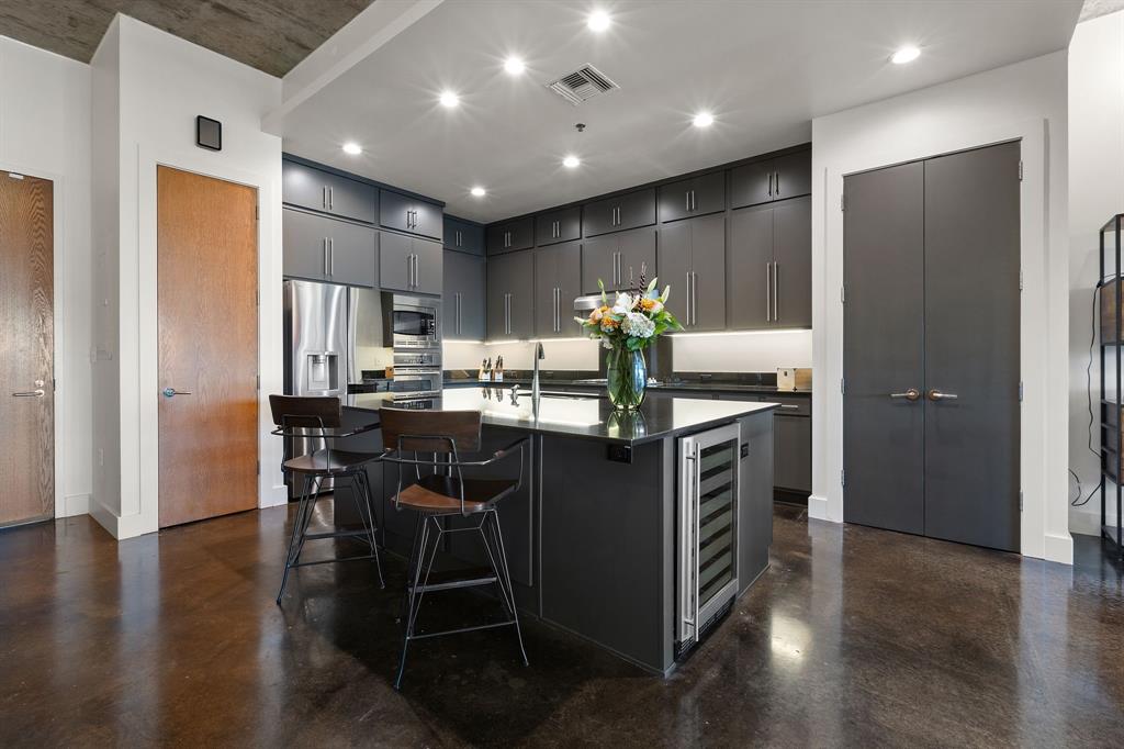 3030 Bryan Street, Unit 409 Dallas, TX 75204 - Photo 2 of 30 a kitchen with kitchen island granite countertop wooden cabinets and a refrigerator