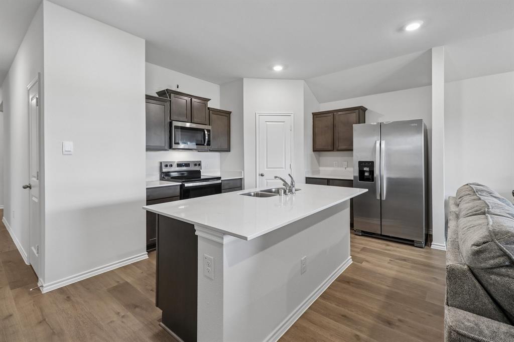 1453 Millstead Rill Road Caddo Mills, TX 75135 - Photo 10 of 40 Kitchen featuring a central island with an integrated sink, white countertops, dark wood cabinetry, and stainless steel appliances including a refrigerator, range, and microwave